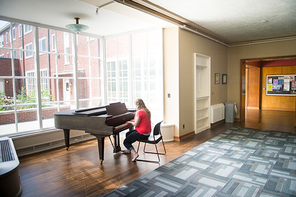 Student playing piano in a Sackett hall lounge