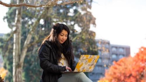 student using laptop on bench outside